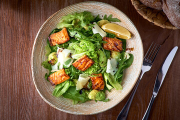 Fresh salad with avocado, arugula and fish fillet, on wooden background close-up. Healthy food.