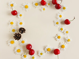 Floral frame with chamomile, cherry berries and fir cones on a ivory background. Top view, Summer flat lay. Empty space for a text or beauty product.