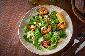 Fresh salad bowl with shrimp, avocado and arugula on wooden background close up. Healthy food.