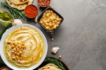 Hummus topped with chickpeas, olive oil and green coriander leaves on stone table with pita bread and spices aside. Flat lay