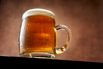 Mug of beer with foam standing against brown background