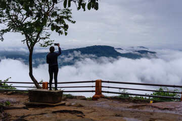 Tourists taking pictures of the scenery at the viewpoint of the cliff That has fog around the...