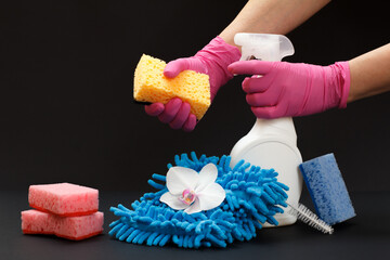 Hands with a sponge and a bottle of washing liquid on a black background.