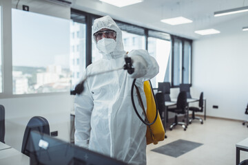 Office disinfection during COVID-19 pandemic. Man in protective suit and face mask spraying for disinfection in the office