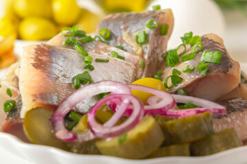 Slices of pickled herring with red onion, fermented cucumber, fried potatoes, olives and boiled eggs on a light wooden table