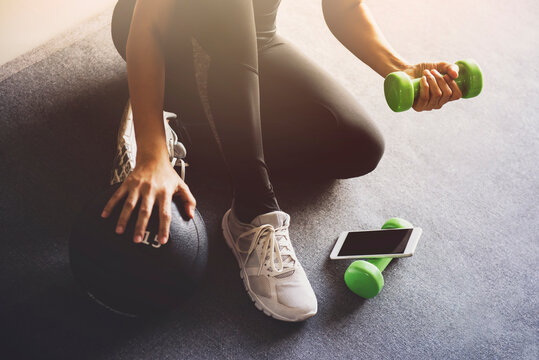 Sporty woman using smartphone during workout at home in the living room.Online personal trainer or on mobile phone.Sport and recreation concept.