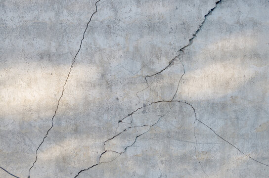 Fragment of gray concrete wall with sun glare and chaotically diverging in different directions, spalls, chips and cracks. Concept: Need to demolish dilapidated buildings and renovate old buildings
