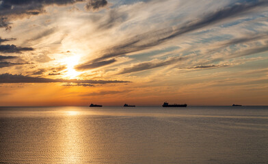 
Summer sunset clouds at sky at Baltic sea on horizon cargo ships going to harbour pink orange sky and sunlight reflection on water wave beautiful nature landscape