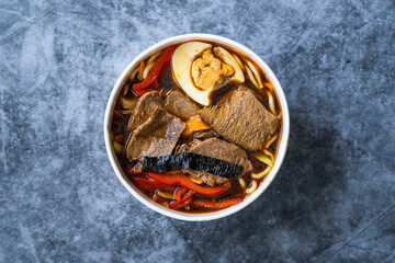 Take Away Shoyu Ramen Noodle with Egg, Soy Sprouts, Veal Meat, Carrot, Onion, Seaweed Wakame, Japanese Radish and Soy Sauce in Plastic Bowl.
