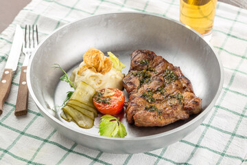 Grilled pork steak with mashed potato, pickles and glass of beer on the table