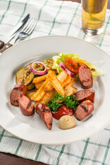 grilled sliced sausage served with beer, french fries, zucchini and ketchup on the side for Octoberfest on the table