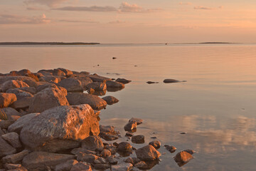 Sunset on the coast of the Baltic sea in Estonia at Haapsalu city with rocks in foreground. rocks and stones on the calm sea and pink sunset sky.