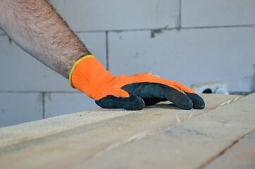 close-up - a man's hand in an orange glove rests on wooden planks