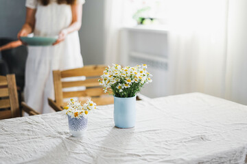 Table with flowers chamomile on linen tablecloth in the living room, bright interior, Cottagecore...