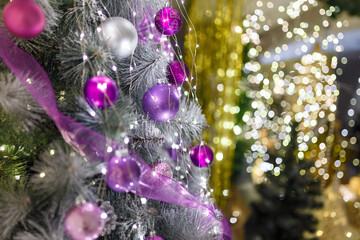 Christmas tree branches with purple decorative bulbs and warm lights bokeh. Shiny sparkling garlands. New Year eve and waiting for miracle concept.