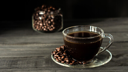 Hot coffee in a coffee cup and roasted coffee beans with a dark tone wood floor. And there is a copy space.