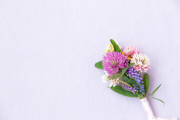 Fototapeta na wymiar Small bouquet of miniature wildflowers on pink background, copyspace for summer and wedding design. Boutonniere from clover and mouse pease wrapped wrapped with ribbon