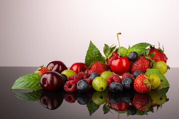 Summer berries on the table with reflection:strawberries,cherries,raspberries,goosberry and blueberry,with fresh minr leaves.
