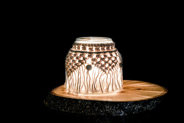 Hand made macrame candle holder on a wooden stand (rustic wood slice), black background.