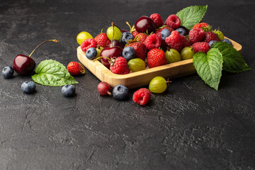 Summer berries in wooden plate:strawberries,cherries,raspberries,goosberry and blueberry,with fresh mint leaves.Copy space.
