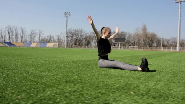 Fit attractive young active woman does yoga stretch pose on huge stadium green grass meditating calmly on warm sunny day