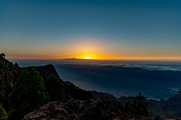 sunset from the canaries, the island of gran canaria with the roque faneque and the teide in the background bathed by a sea of clouds and the reflections and lux of the sun, in tamadaba natural park.
