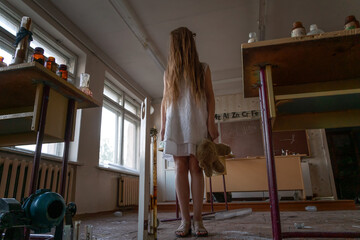 girl in a white dress with long hair and a Teddy bear in her hands stands in an abandoned chemistry room in an old ruined school. Concept of horror, mysticism