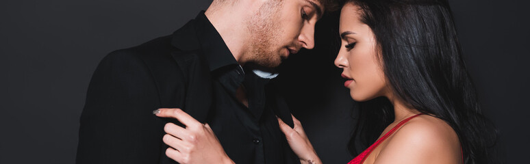 panoramic shot of sexy woman touching shirt of handsome man isolated on black