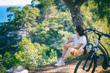 The girl has a rest in the forest with a bicycle, enjoys nature and loneliness. Summer vacation and travel, bicycle, sports and outdoor activities.