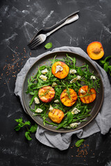 Fresh diet salad grilled peach, arugula and blue cheese in a plate on a black stone background. Top view, flat lay.