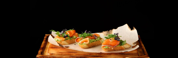 Selection of tasty bruschetta or canapes with salmon banner closeup. salmon tapas with guacamole and topped microgreen
