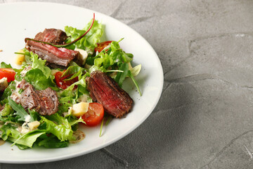 steak salad. Grilled Steak with Mixed Greed Salad cherry tomatoes and parmesan with fresh sauce in white plate on concrete background