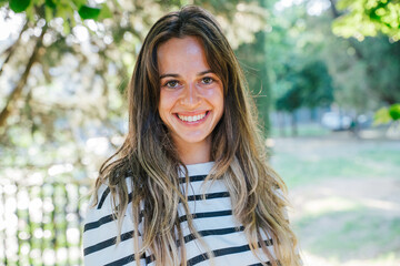 Portrait of a young beautiful blonde woman in the park in summer - Millennial outdoor in a moment of relax looking the camera and smiling