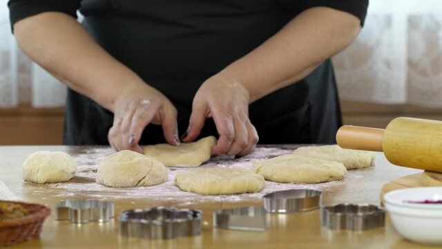 Close-up women's hands knead dough baking pastry at home, preparing pizza or handmade danish cookies. DIY bakery, baking moulds and rolling pin on table sprinkled with flour.