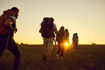 Hike. Hiking. Tourism.A group of tourists with backpacks are walking along the hill at sunset in...