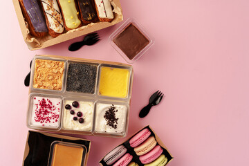 Carton boxes with eclair cakes and cookies on pink surface