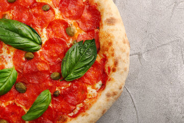 pepperoni pizza with capers and basil closeup on light concrete or stone table or background