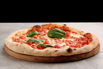 pizza with bacon and cherry tomatoes and basil on light concrete or stone table with black background for copy space