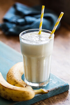Vegan friendly banana and soya milk smoothie in tall glass served on blue napkin on rustic wooden table