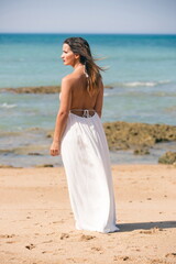 Fototapeta na wymiar Woman in white dress and back to the air standing on the beach