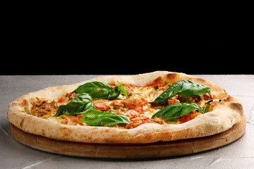 pizza with tuna mozzarella, onion and basil closeup on light concrete or stone table and black background for copy space