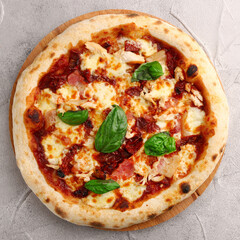 pizza with dried tomatoes, chicken, basil, tomatoes and mozzarella cheese close up on gray concrete or stone table top view