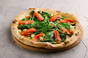 salmon pizza with spinach close up on gray concrete or stone table. seafood italian pizza top view
