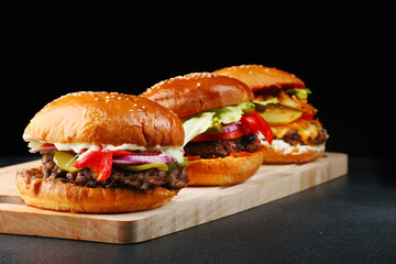 set of three burgers close up on wood and black isolated background for copy space. big tasty and juicy burgers concept