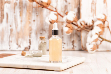 Fototapeta na wymiar Mockup of moisturizing essence in a dropper glass bottle on a marble tray and wooden table. Cosmetic or spa skincare concept, cotton branch