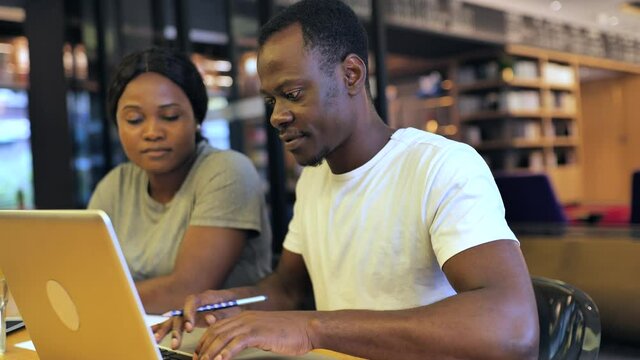 Close up of two Black college students study discussion together using laptop indoor one African Businessman freelancer explaining communication with his female partner in cafe