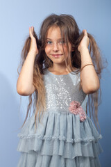 Naklejka premium A beautiful long-haired girl with her favorite items in her hands on a light background in a gray dress with sequins. Foreground. Quarantine, games at home.
