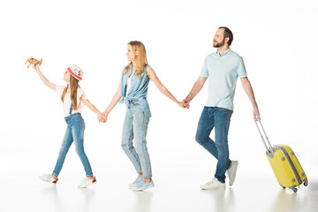 Naklejka premium happy family holding hands while walking with travel bag isolated on white