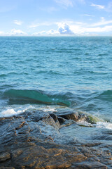Water splashing. Crystal clear sea water beating against the rocks and cliffs. Blue sky above the beach in the sun zenith refreshing drops of ocean water. Sea waves break on the shore after a storm