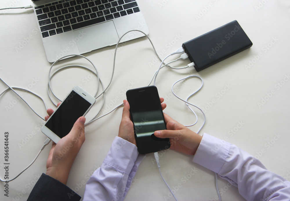 Poster two people using two mobile phone sharing usb power bank on a table to charge the mobile devices.tec